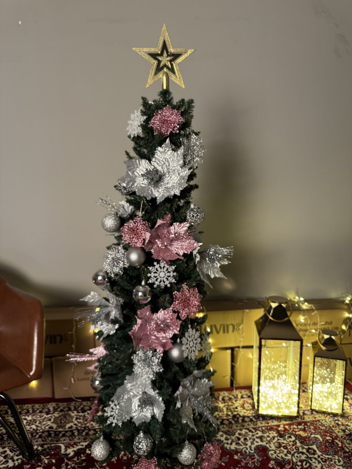 Árvore slim de 1,50 m decorada com flores rosa e prateadas, bolas e estrela dourada, com lanternas e luzes ao lado