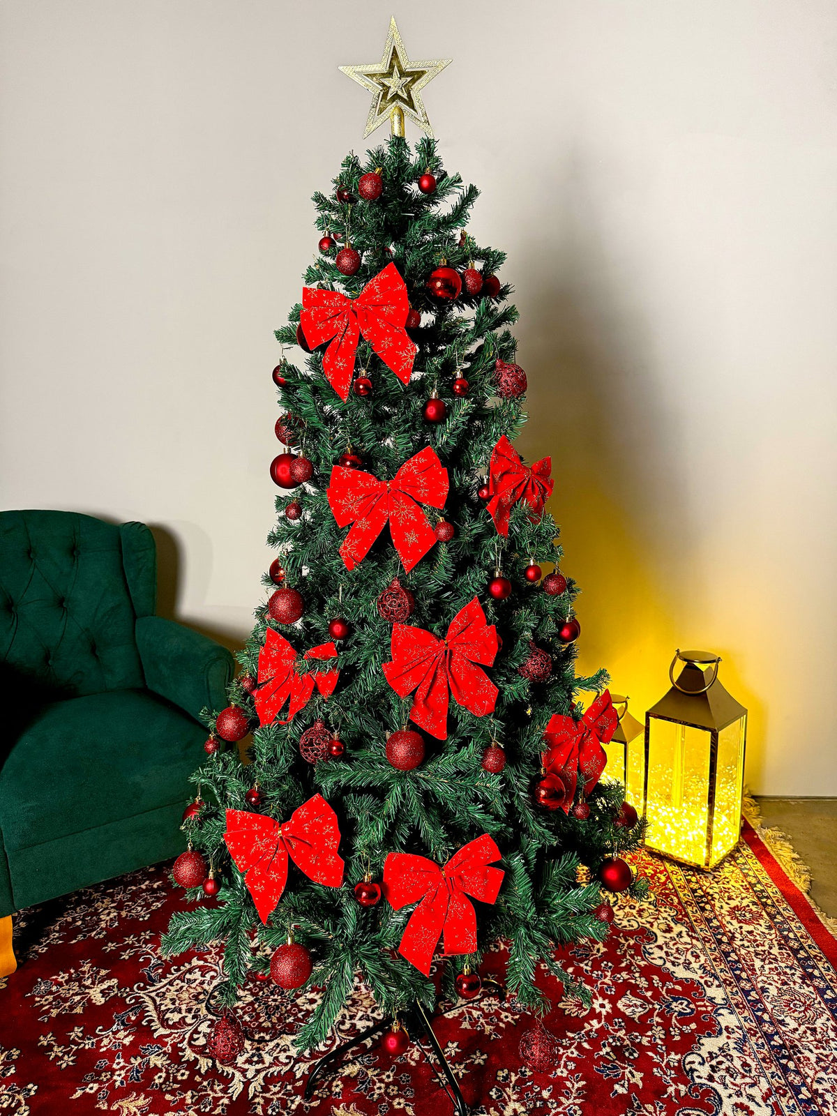 Pinheiro canadense tradicional de 1,80 m decorada com laços vermelhos, bolas e estrela dourada, ao lado de poltrona verde e lanterna