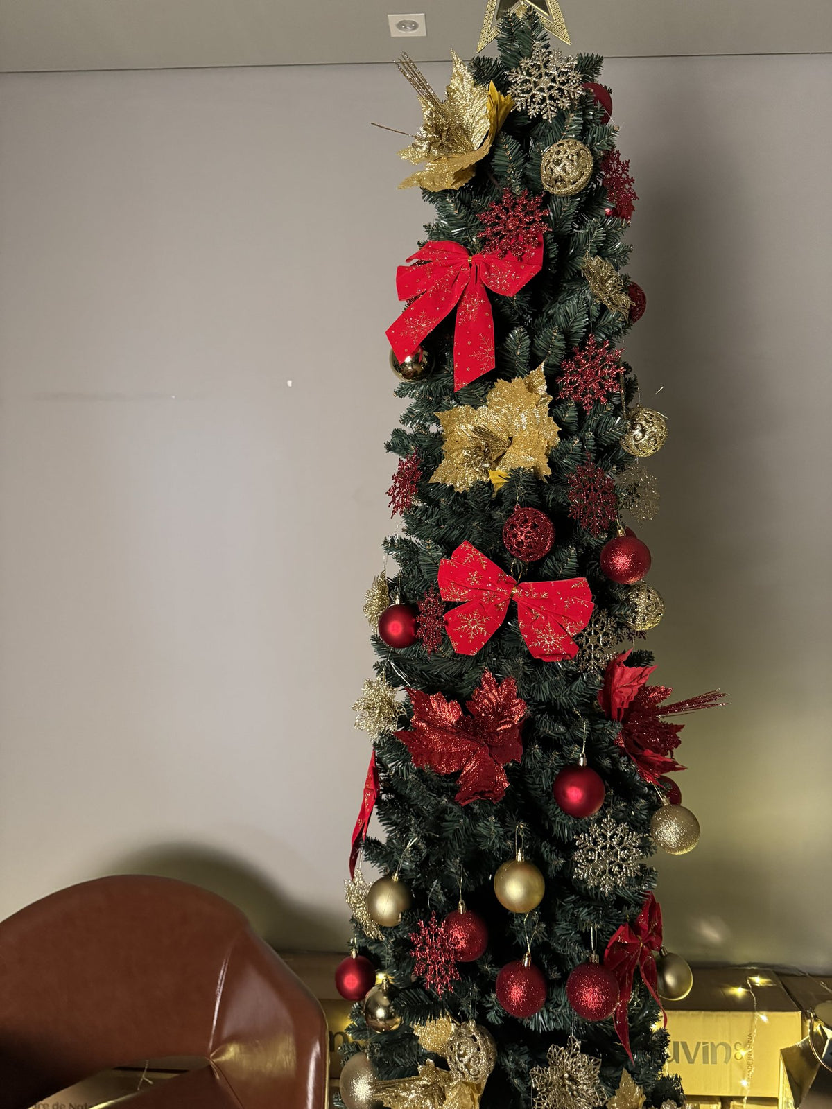 Árvore slim de 2,40 m decorada com laços vermelhos, flores e bolas douradas, com lanternas e luzes ao lado