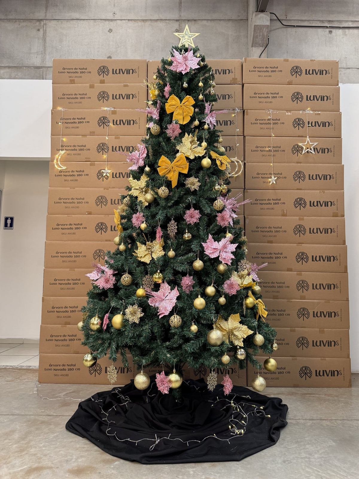 Pinheiro canadense tradicional de 2,70 m decorada com flores e laços rosa e dourados e estrela, em frente a caixas empilhadas