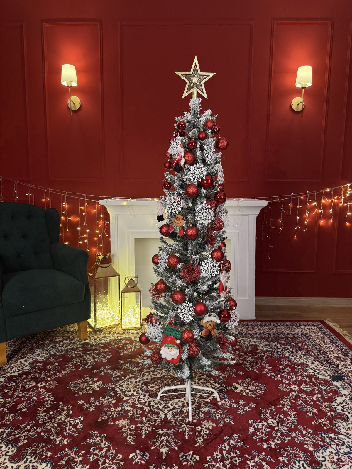 Árvore slim nevada de 1,50 m decorada com bolas vermelhas e prateadas, estrela dourada e luzes, em sala com parede vermelha e lareira