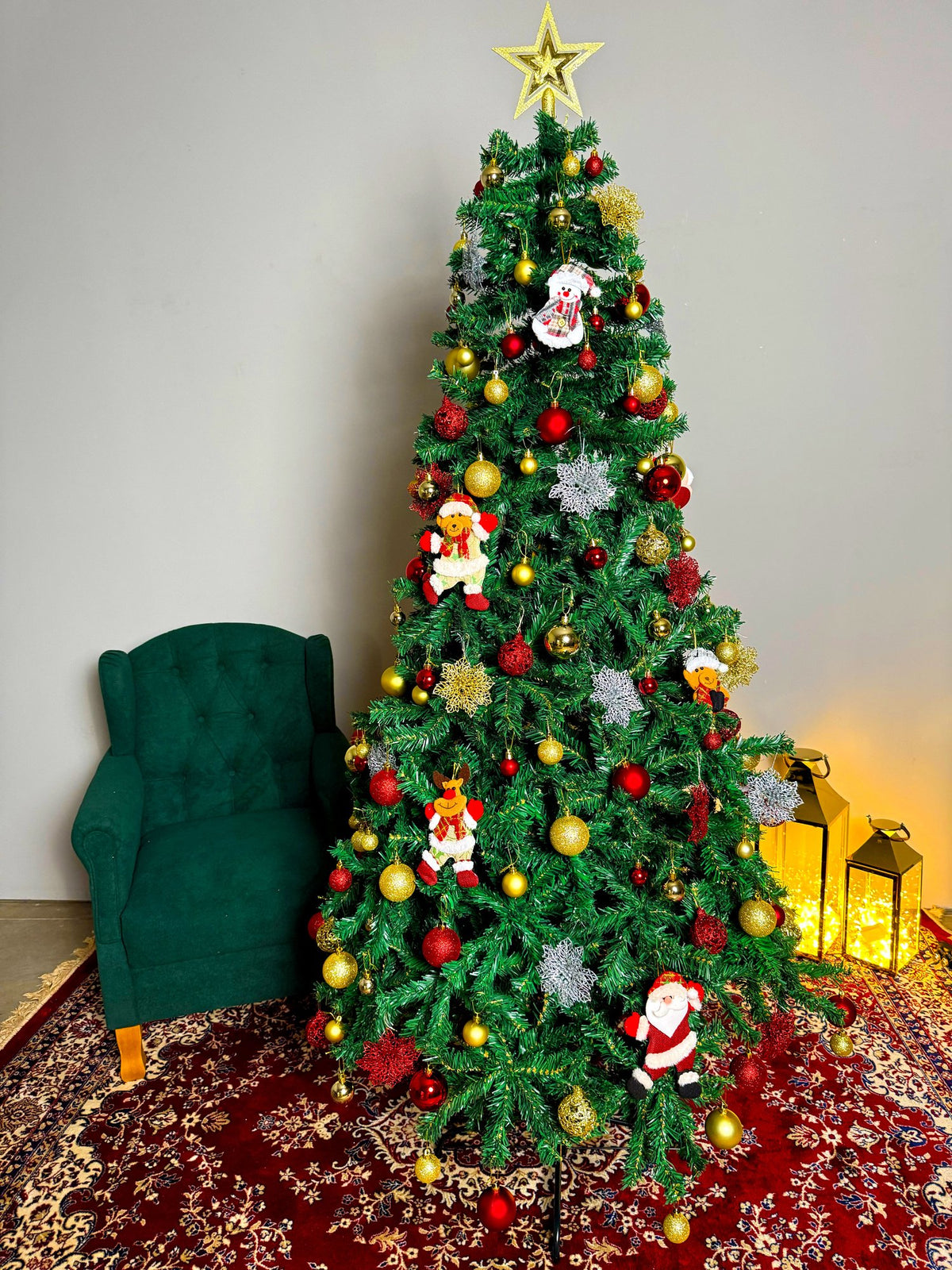 Pinheiro canadense tradicional de 2,10 m decorada com Papais Noéis, bolas vermelhas e prateadas, luzes e estrela dourada, ao lado de poltrona verde