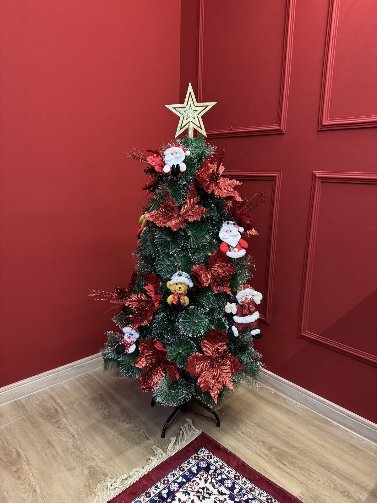 Árvore pompom com pontas nevadas de 1,20 m decorada com flores vermelhas, bonecos de Papai Noel e estrela dourada, em sala com parede vermelha