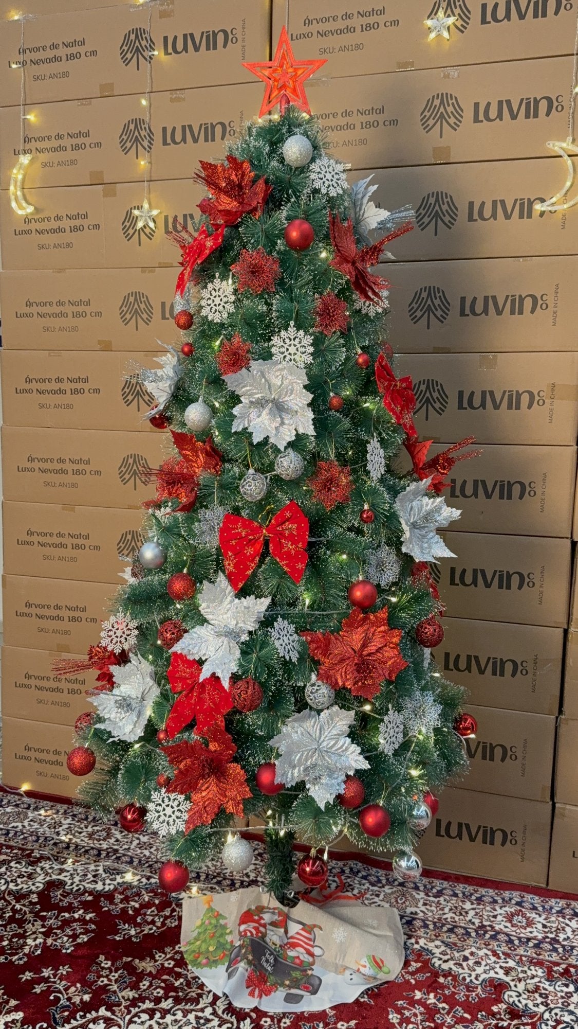 Árvore pompom com pontas nevadas de 2,10 m decorada com laços e flores vermelhas e prateadas, com saia de árvore estampada