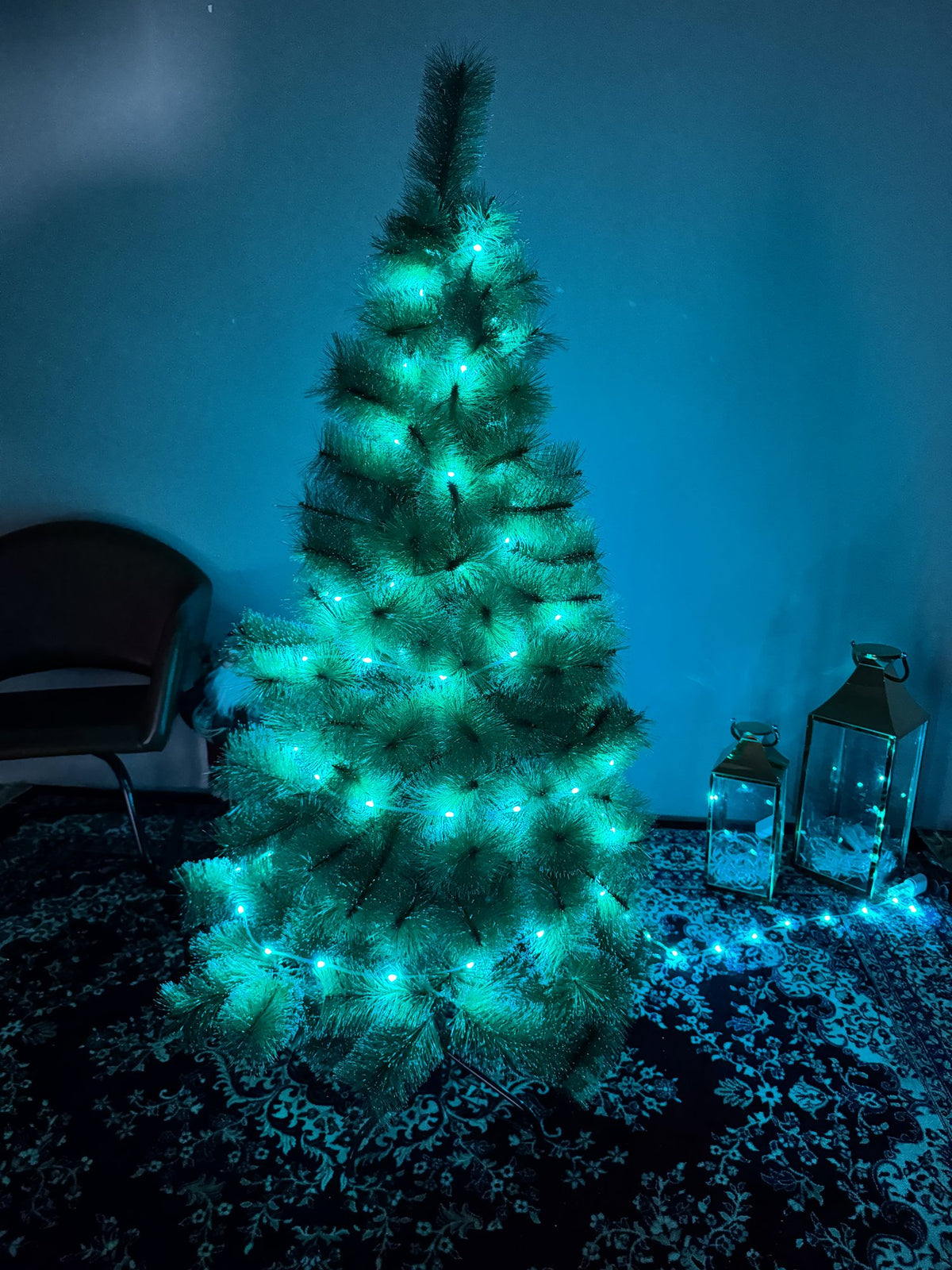 Árvore pompom com pontas nevadas de 1,50 m com pisca-pisca de luz azul-turquesa em ambiente escuro